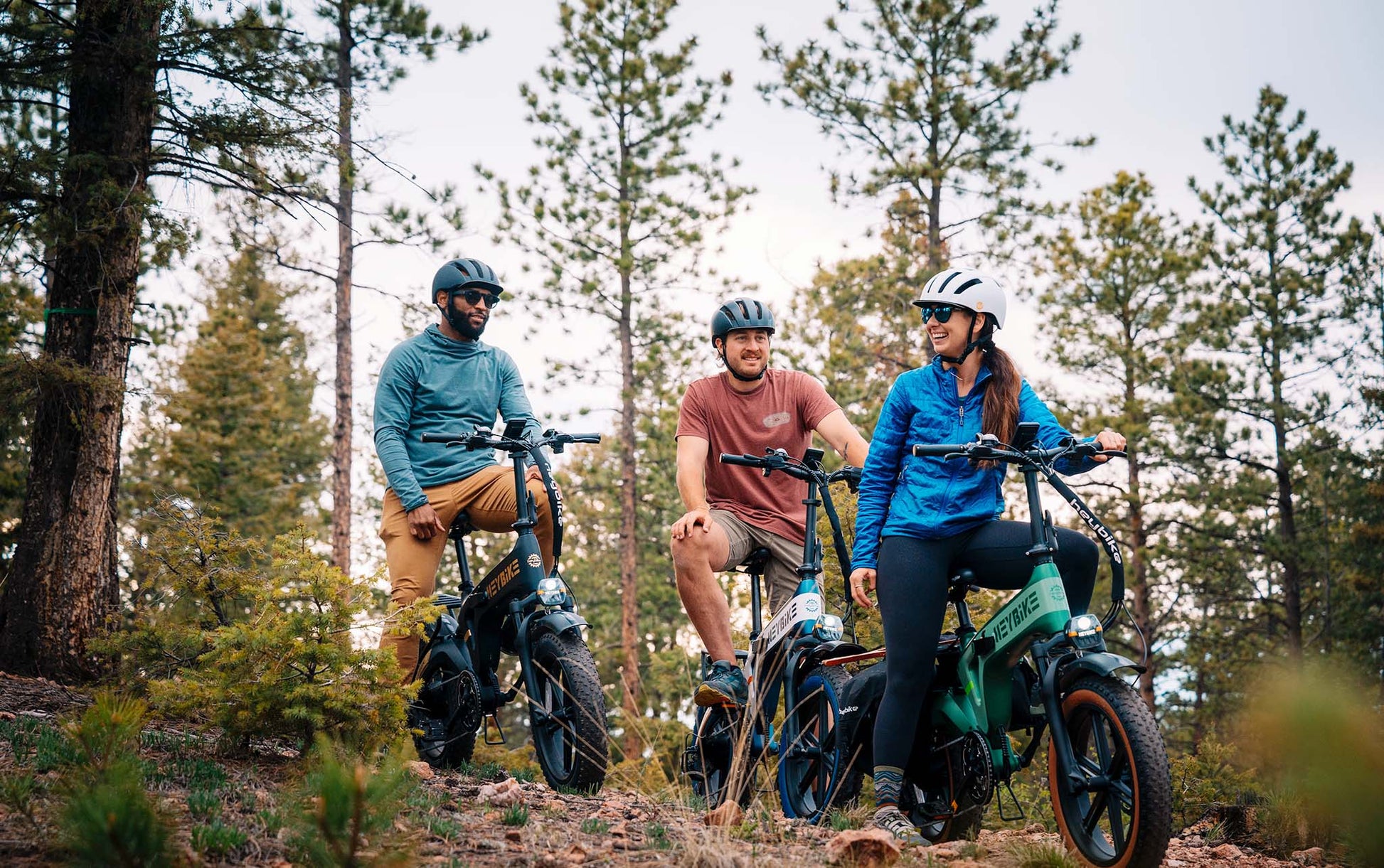 Three people riding HEYBIKE Tyson ebikes in a forest setting.